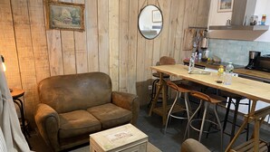 A cozy living room with a brown leather sofa, a wooden dining table with bar stools, a small wooden chest, and a mirror on the wall. - Charming Valentine fisherman's cottage, town center, close to train station and beach (Trouville-sur-Mer)