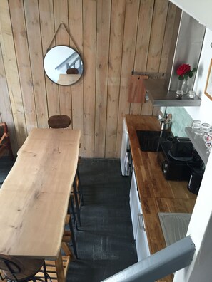 Una cocina compacta con paredes de madera, un espejo redondo, una mesa de madera y una encimera con diversos utensilios de cocina.