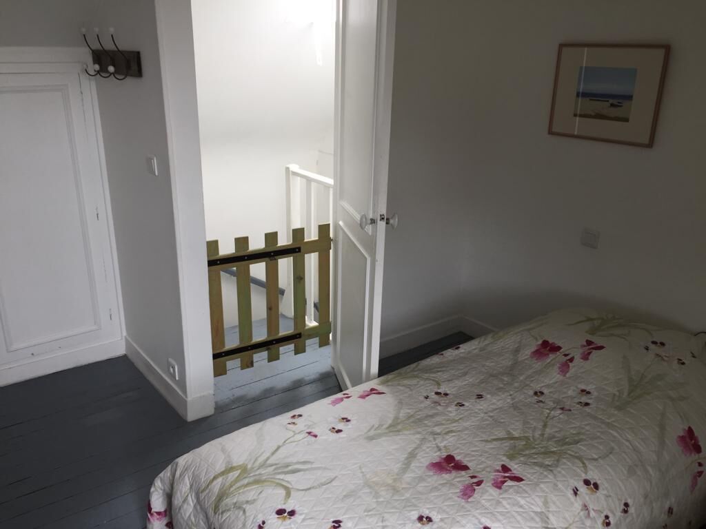 A bedroom with a bed, a door, a staircase, and a framed picture on the wall.