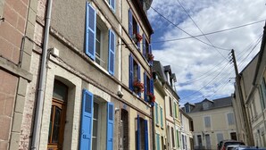 A narrow street lined with multi-story buildings featuring traditional architecture, a row of parked cars, and visible utility poles. - Charming Valentine fisherman's cottage, town center, close to train station and beach (Trouville-sur-Mer)