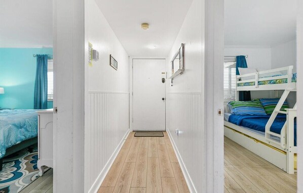A narrow hallway with a wooden floor, white walls, and a door at the end.