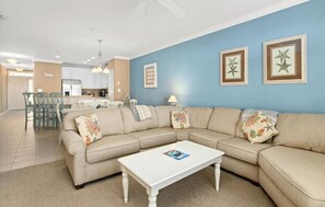 Una sala de estar con un sofá seccional color beige, una mesa de centro blanca y una pared de acento azul.