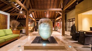 Un vestíbulo amplio con un gran jarrón decorativo, vigas de madera y un sofá verde.