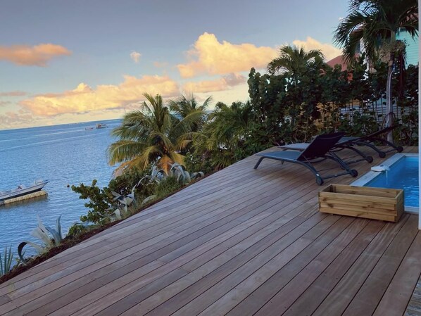 A wooden deck with a pool, lounge chairs, and a view of the ocean.
