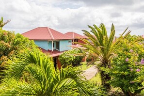 A house with a red roof and a blue exterior, surrounded by lush greenery and flowering plants.
