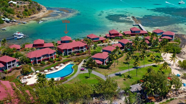 Vista aérea de un resort con varias villas de techo rojo, una piscina central y una zona de playa.
