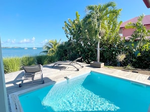 A swimming pool with a view of the sea, surrounded by palm trees and a wooden deck.