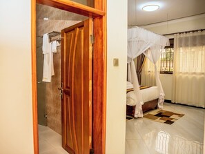 Een slaapkamer met een houten deur, een bed met hemelbed en een badkamer met handdoekhouder.
