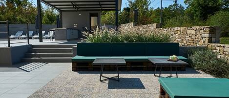 Un patio al aire libre con un muro de piedra, un banco verde y una mesa con mantel verde.