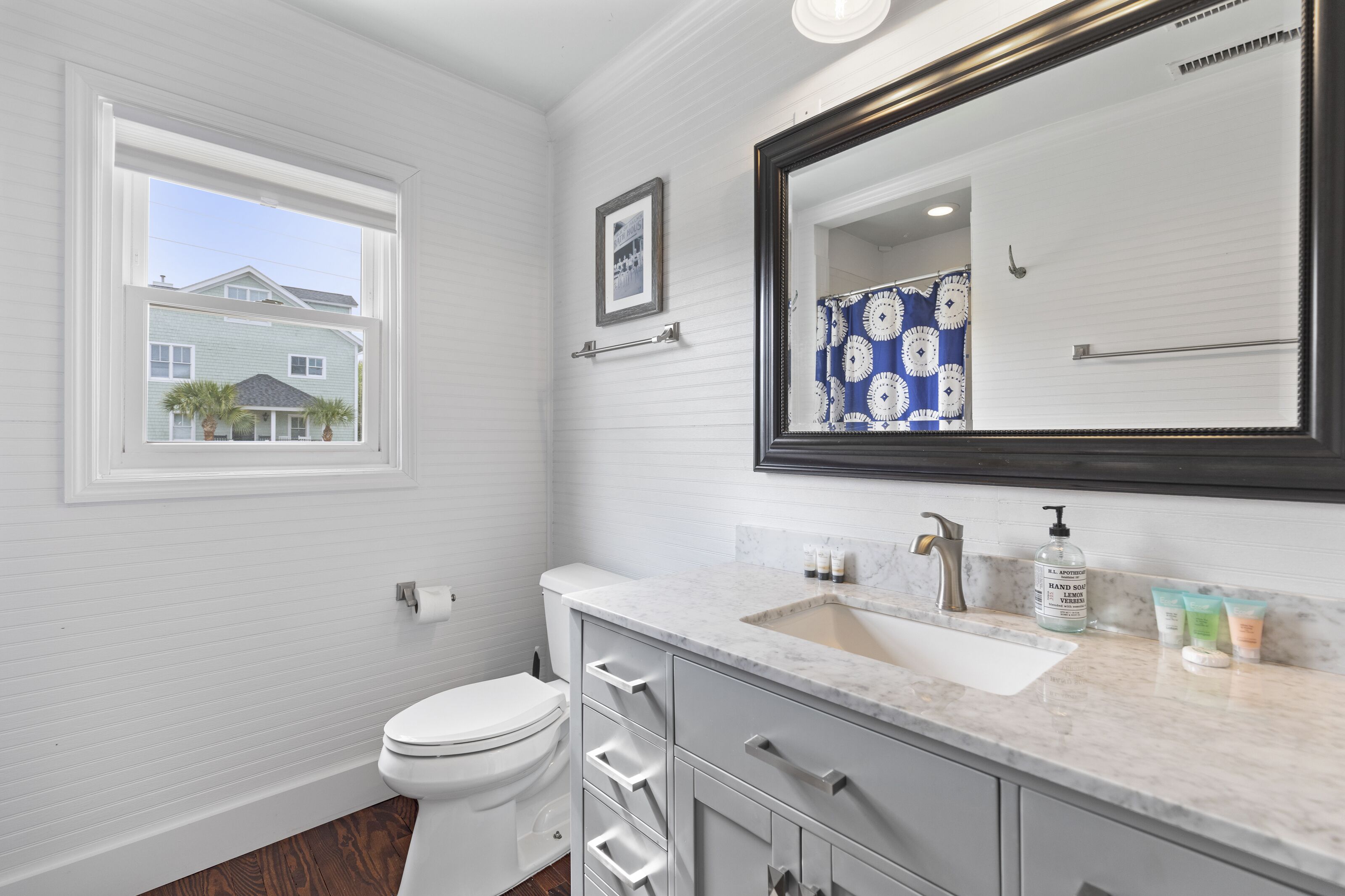 A bathroom with a toilet, sink, vanity, and a large mirror.