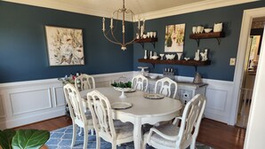 A dining room with a round table, white chairs, a chandelier, and decorative shelves with white pottery.