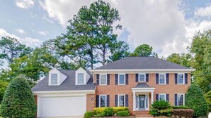 A two-story brick house with a white garage door, a front porch, and a well-maintained lawn.