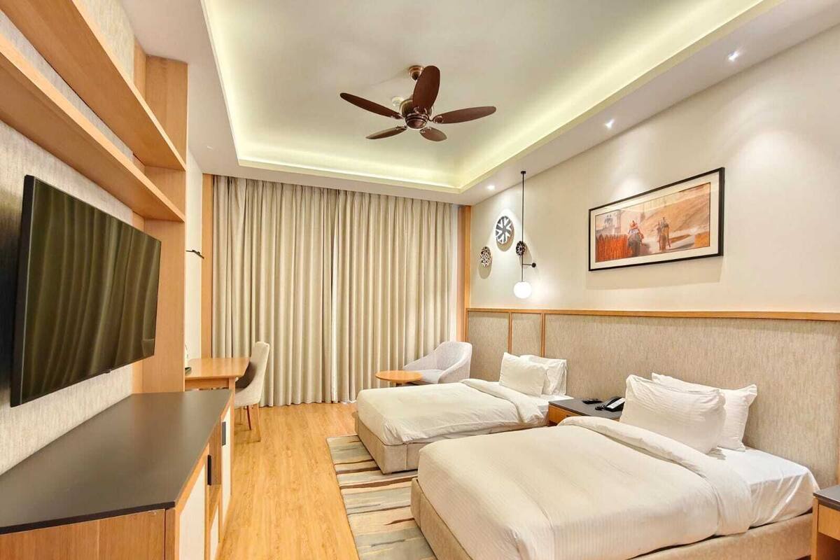 A hotel room with a bed, a desk, a chair, a ceiling fan, and a TV.