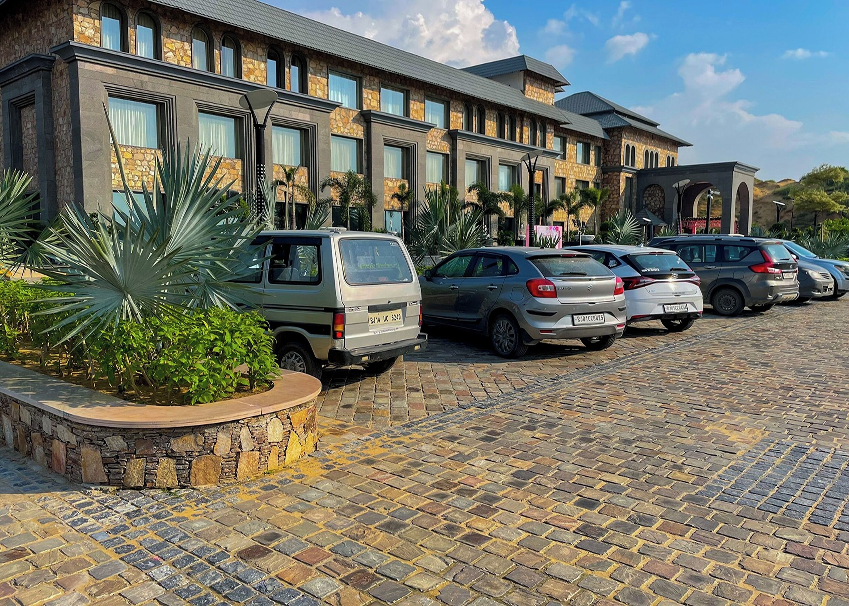 Ein Hotel mit einer Stein-Fassade, geparkten Autos und einem Kopfsteinpflaster-Zugang.