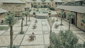 Une cour bordée de bâtiments en pierre, de palmiers et dotée d’un espace piscine central.