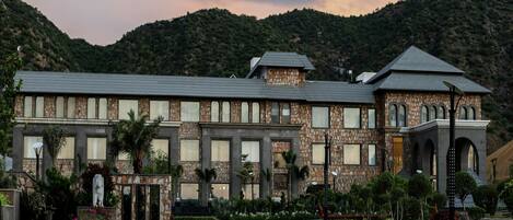 A stone building with a courtyard, surrounded by greenery and hills.