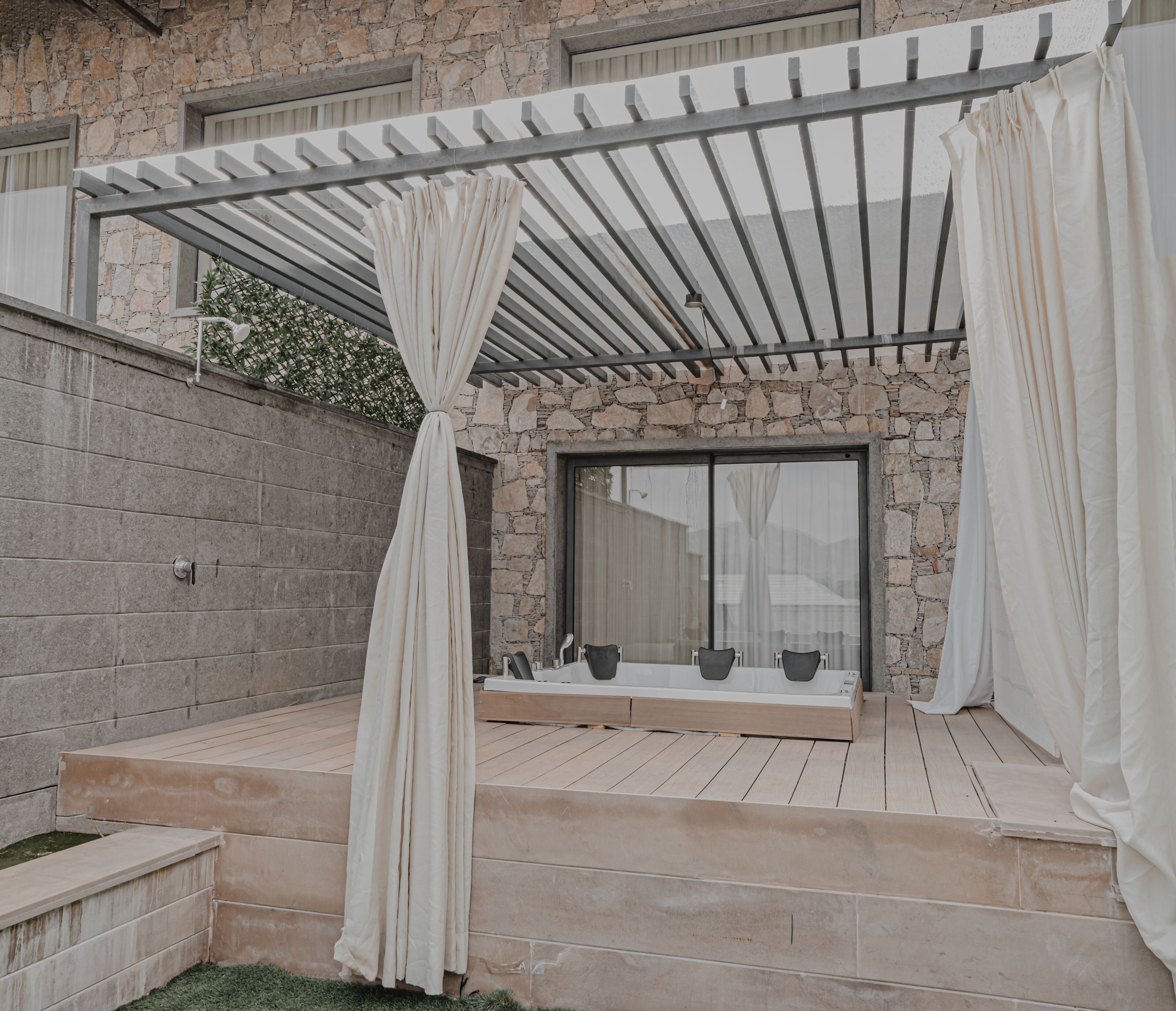 A covered outdoor area with a stone wall, a wooden deck, and a seating area with chairs and a table.