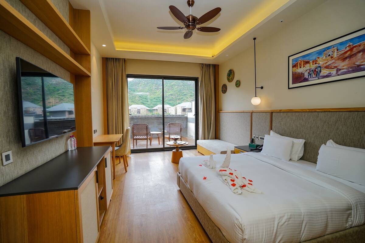 A hotel room with a bed, a desk, a chair, a television, and a balcony with a view of greenery.