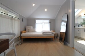 Ein Schlafzimmer mit Bett, Sessel, Nachttisch, Spiegel und einem Fenster mit Vorhängen.