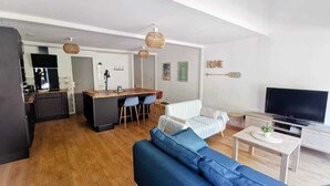 A modern living room with a blue sofa, a TV, and a dining area with a kitchen in the background.