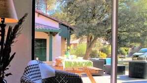 A room with a large window, a patterned chair, and a table set outdoors with a green tablecloth.