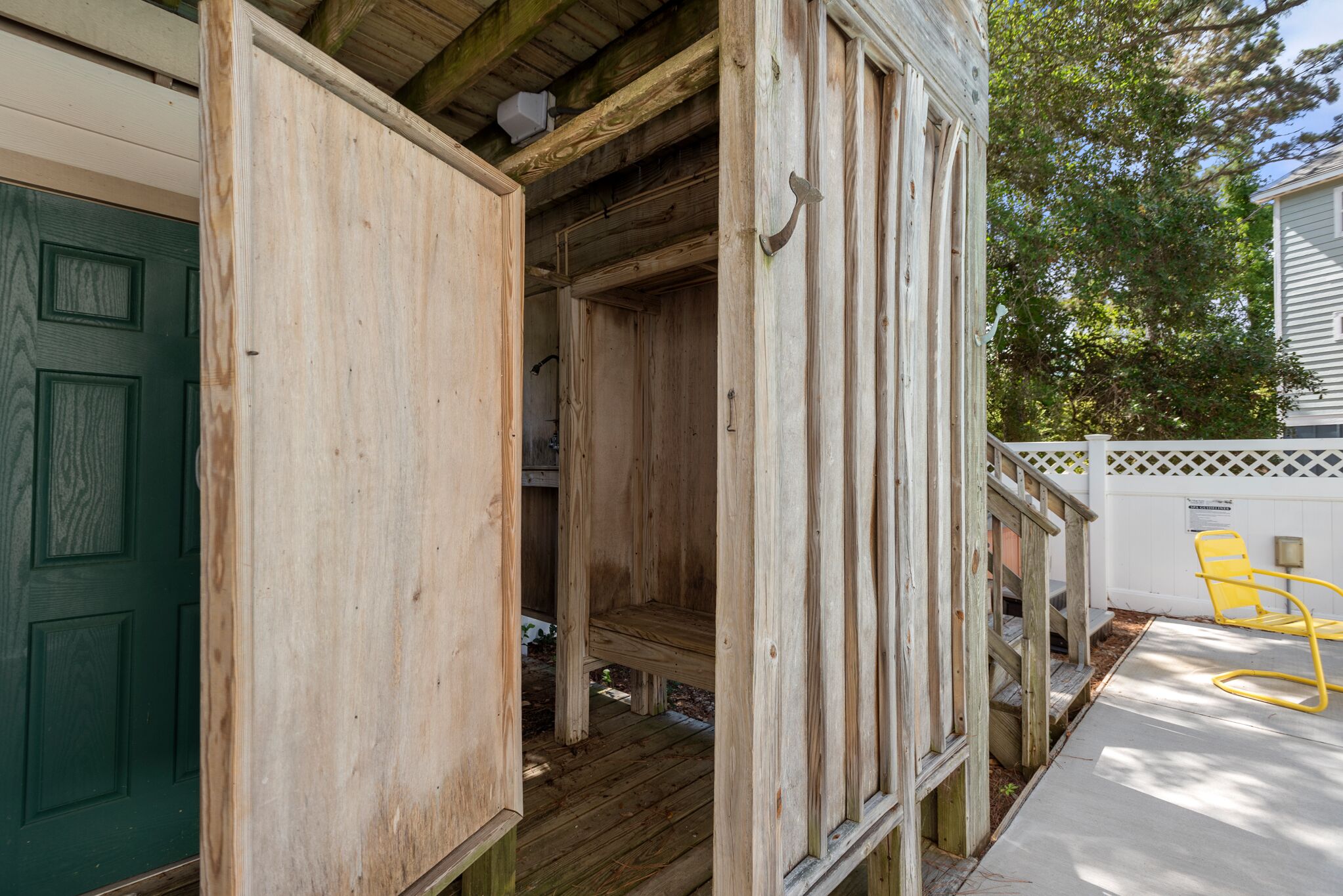 Een houten constructie met een deur, een bankje en een gele stoel ernaast.