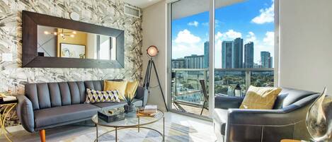 A modern living room with a large sofa, a coffee table, and a view of a city skyline through large windows.