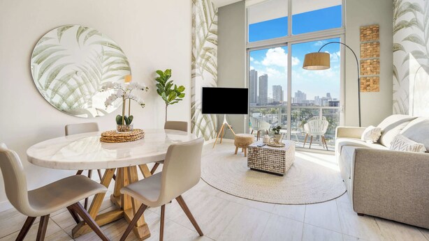 A modern living room with a round dining table, white chairs, a sofa, and a large window with a city view.