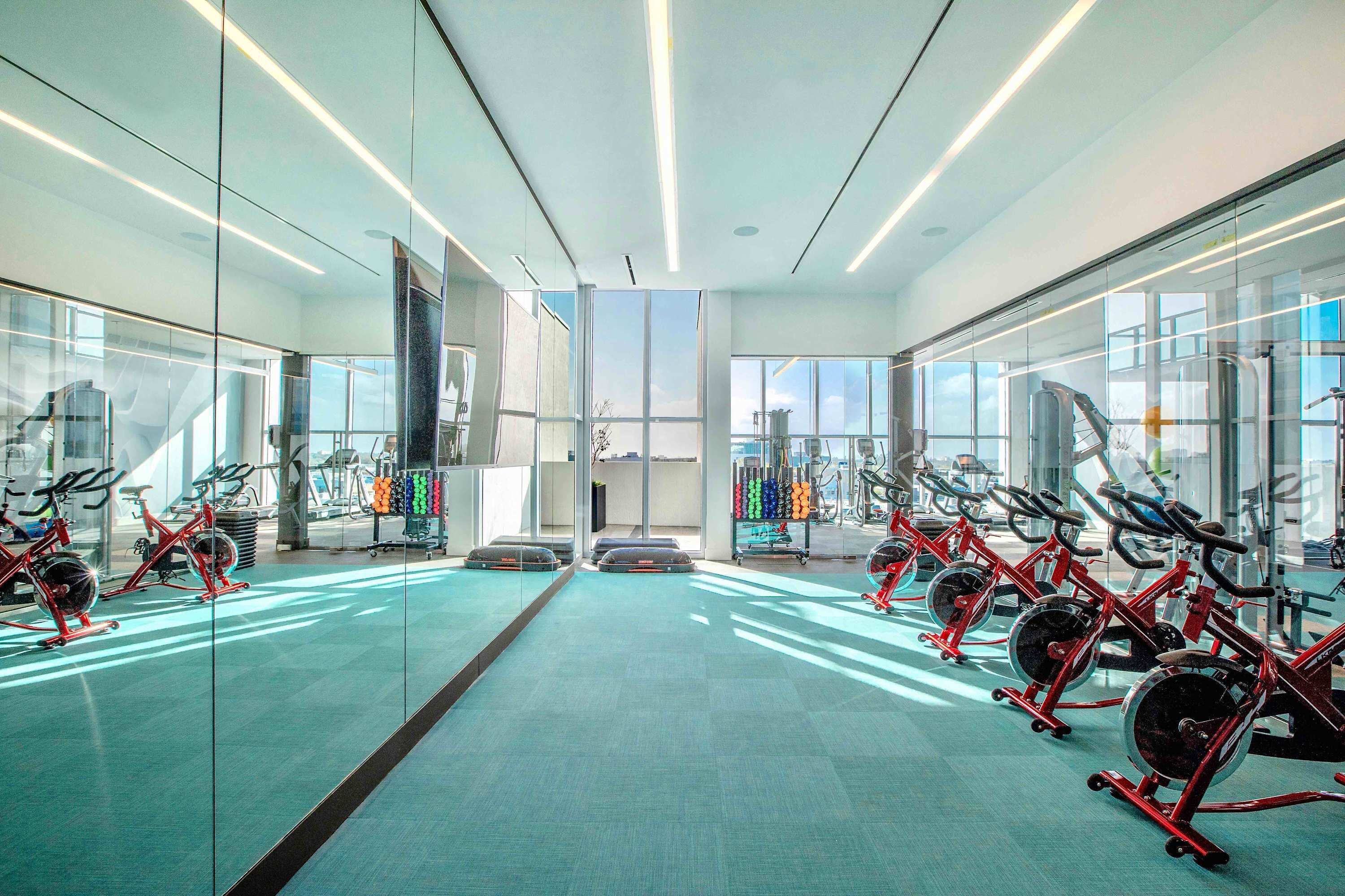 A modern gym with rows of stationary bikes, large windows, and a spacious layout.