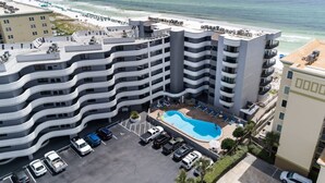 A multi-story hotel with a rooftop pool, parking area, and ocean view.