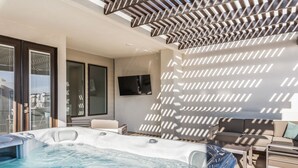 Uma área externa moderna com hidromassagem, um sofá e uma TV fixada na parede.