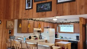 Une cuisine aux murs lambrés, dotée d’un îlot central, de tabourets de bar et de tableaux encadrés.