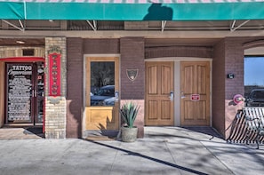 Un edificio con un letrero de Piercing & Tattoo, una puerta corta fuegos y un banco.