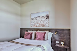 Una cama bien tendida con tablero de madera, dos almohadas rosas y una colcha blanca.