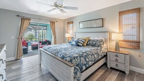 Un dormitorio con cama, mesita de noche, ventilador de techo y vistas a un área de estar exterior a través de una puerta de cristal.
