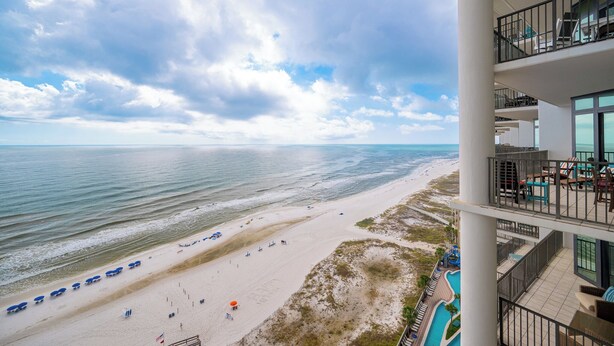 A beach view from a hotel balcony with a pool and outdoor seating.
