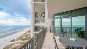 A balcony with a view of the beach and ocean, a table with chairs, and a railing.
