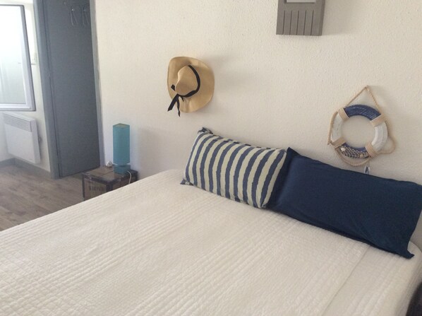 Un lit bien fait, avec des oreillers à rayures et d’autres de couleur unie, un chapeau accroché au mur et un anneau de sauvetage.