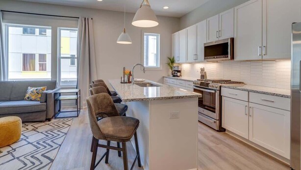 Une cuisine moderne avec des meubles blancs, un îlot central, des appareils en acier inoxydable et des luminaires suspendus.