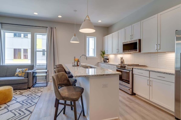 A modern kitchen with white cabinets, a central island, stainless steel appliances, and pendant lighting. - double deck: 2 nashville homes, sleeps 24, on VRBO (Nashville)
