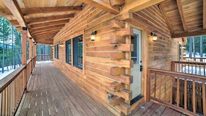 Eine Holzhütte mit einer Veranda, großen Fenstern und einer Tür mit einer kleinen Sitzterrasse.