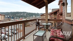 A balcony with wicker furniture, a glass table, and a view of a parking lot and buildings.