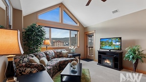 A living room with a sofa, a TV, a fireplace, and a large window with a view of the outdoors.