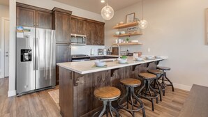 Una cocina moderna con refrigerador de acero inoxidable, armarios de madera, una isla central con taburetes e iluminación colgante.