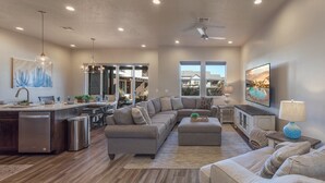 Un amplio espacio de sala con un sofá modular grande, una mesa de comedor y una cocina equipada con lavavajillas y pileta.