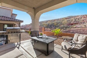 Une terrasse extérieure équipée d’un barbecue, de sièges et offrant une vue sur un paysage vallonné.