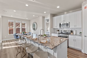 A modern kitchen with white cabinets, a granite countertop, stainless steel appliances, and a dining area with bar stools. - Escondido 2343 & 2355 Retreat, Connected homes with 10 Bedrooms, sleeps 40, and endless amenities (Washington)