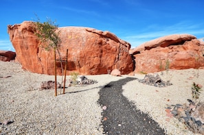 A desert landscape with large red rock formations and a gravel path leading towards them.