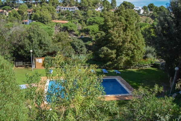 A residential area with a swimming pool surrounded by lush greenery and a view of houses in the background.