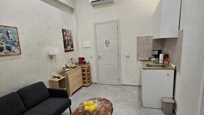 A compact living space with a sofa, a coffee table with lemons, a kitchenette, and a door with a no smoking sign. - Alloggio Turistico Port Inn (Civitavecchia)